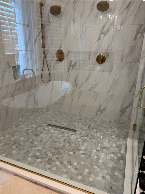 Walk-in shower with brass fixtures and marble hex floor
